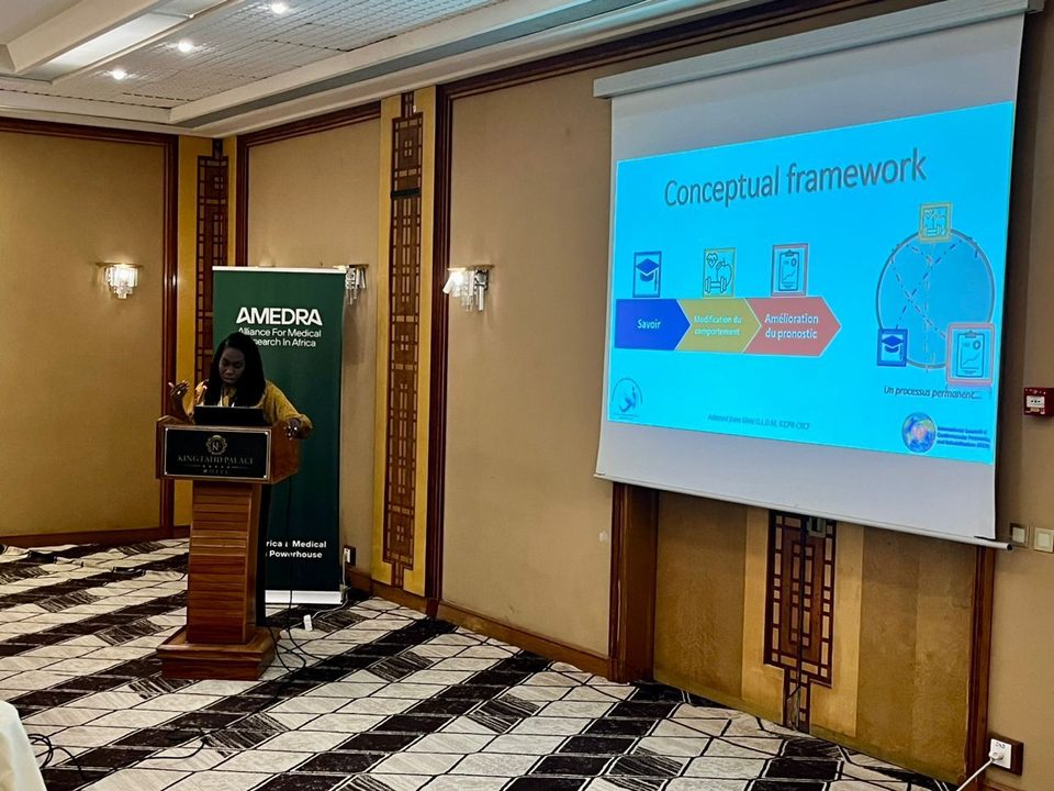 A presenter at the podium beside the AMedRA banner at King Fahd Palace, Dakar